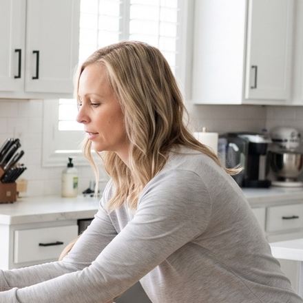 A woman standing calmly in her kitchen in the morning light.